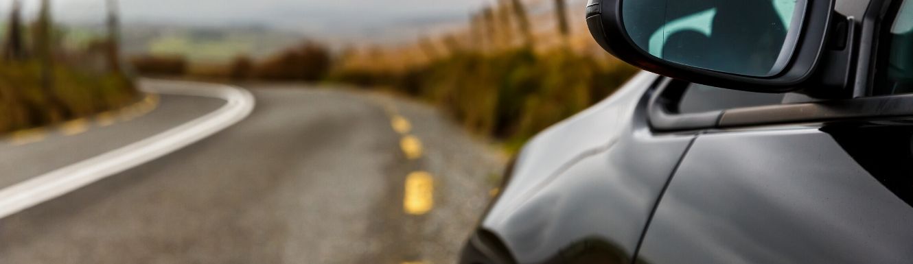 Car traveling down road with close up of driver's side mirror