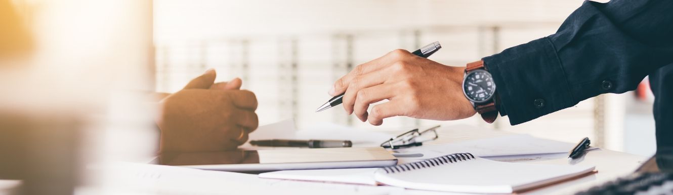 Man's hand holding pen above desk strewn with financial statements