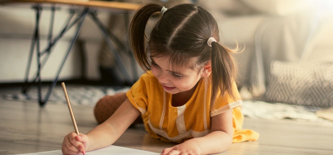 little girl laying writing on a paper while laying on living room floor