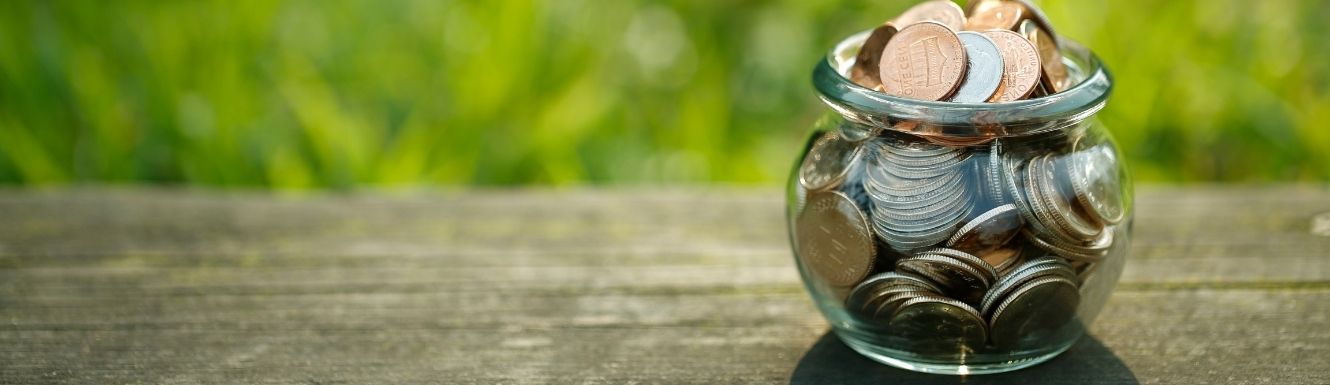 Glass cauldron-shaped bowl filled with U.S. coin currency on top of an outdoor wooden table.