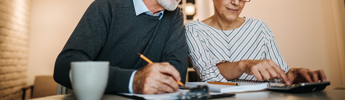 Retired couple using calculator while reviewing financial statements