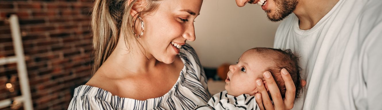 young couple holding, looking down at and smiling at newborn baby