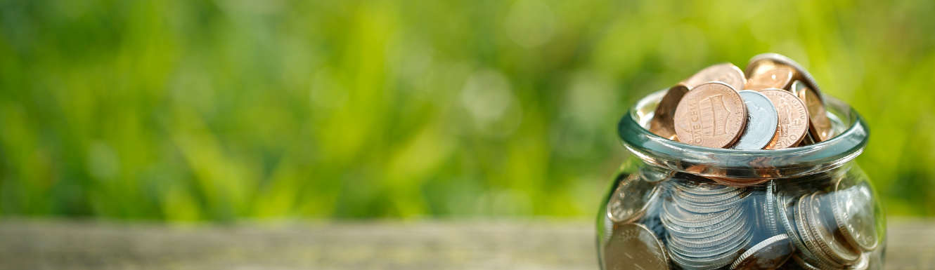 jar of coins sitting on table with green plants blurred in background