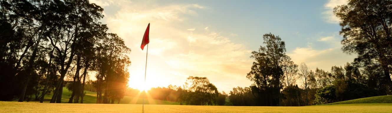 Flag in the hole on golf course with sun setting